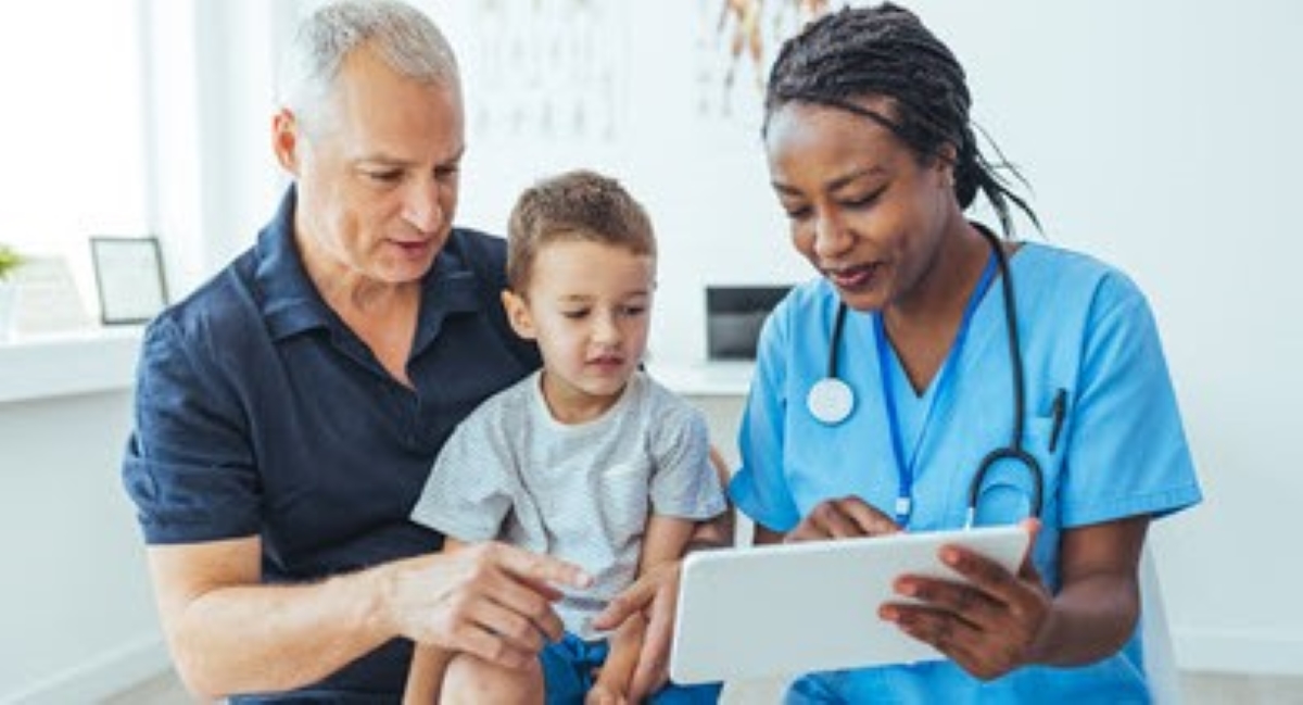 A doctor interacts with a young boy in a medical office, discussing health while seated on an examination table.