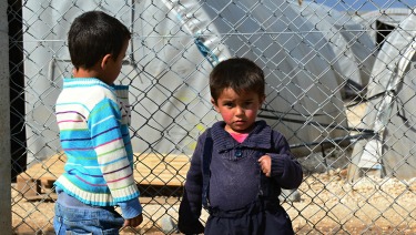 Two refugee children standing by a fence.