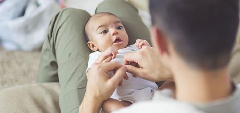A parent interacts with a baby sitting on their lap, both looking engaged and playful in a cozy setting.