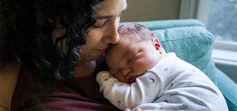 A mother gently cradles her sleeping baby in her arms, both looking peaceful in a cozy setting.