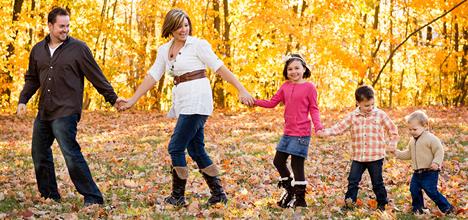 A family walks hand-in-hand through a colorful autumn landscape, surrounded by orange and yellow leaves.