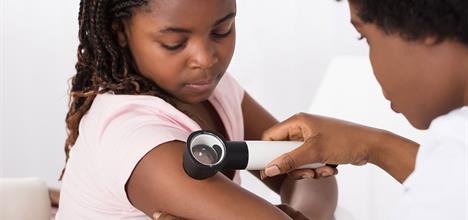 A healthcare professional examines a child's arm with a magnifying tool in a clinical setting.