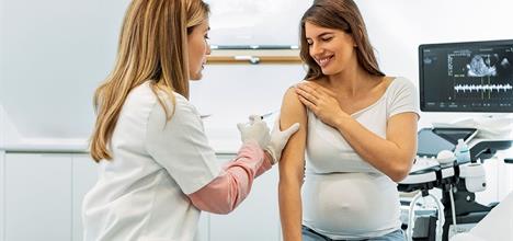 A healthcare professional administers a vaccine to a pregnant woman in a medical setting.