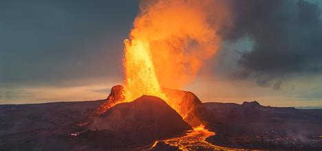 A volcano erupts, spewing lava and ash into the sky, with glowing lava flows visible on the ground.